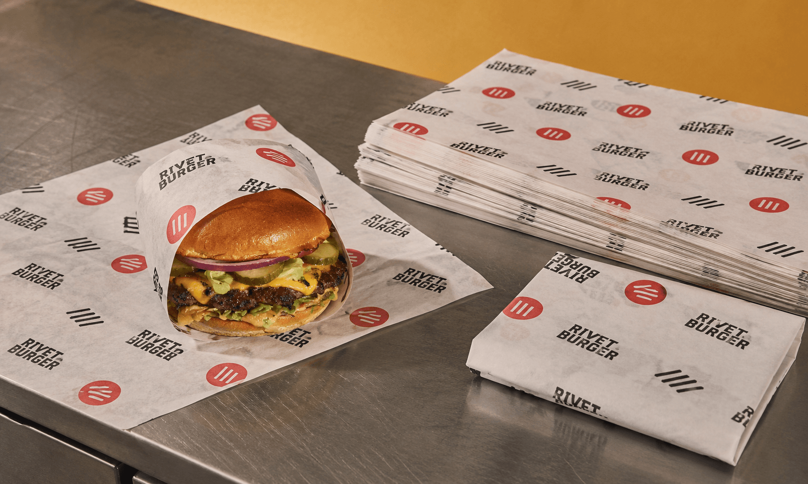 Custom printed wax paper sheets beside a wrapped burger and pastry on a refined food-service counter