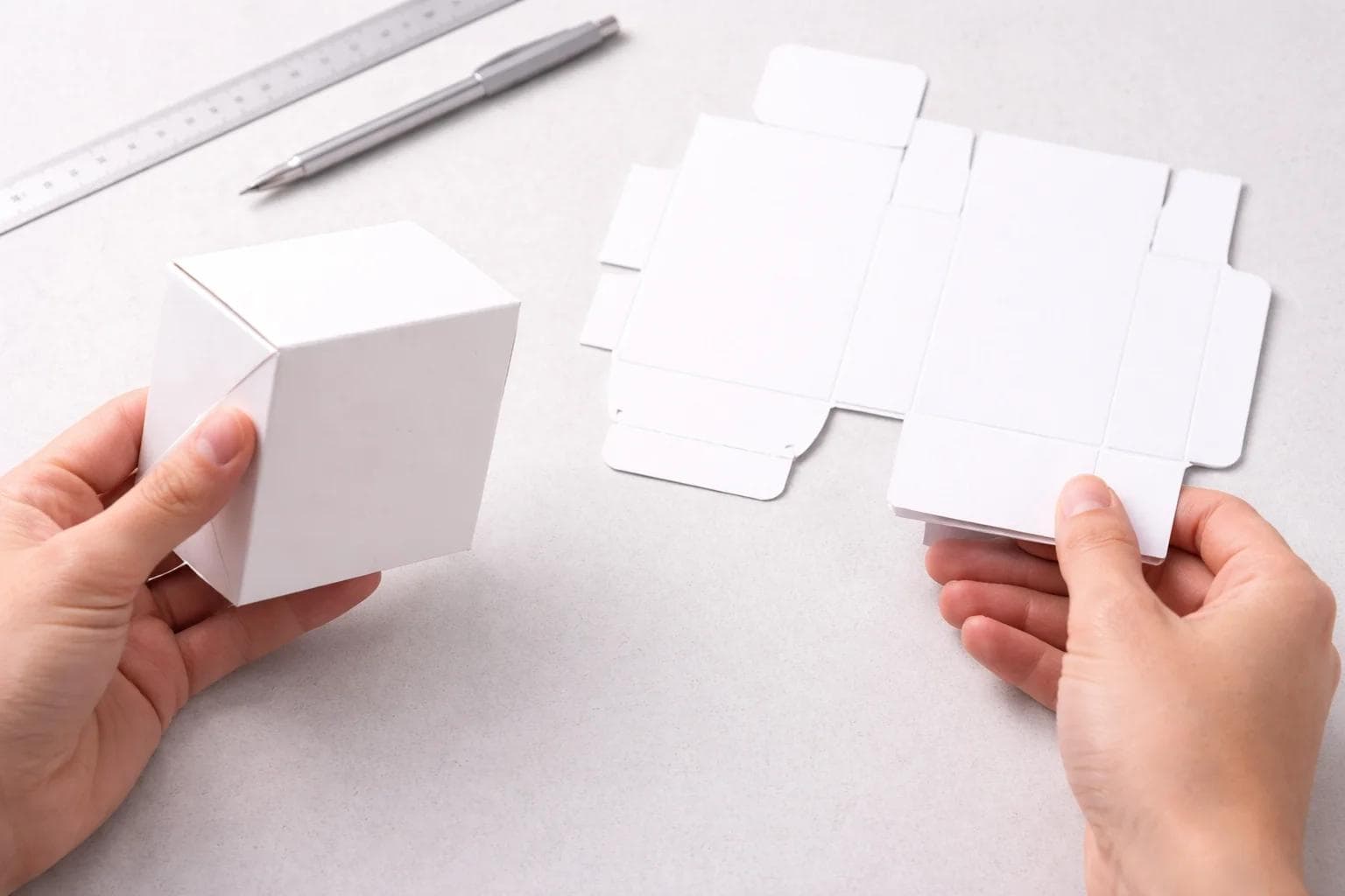 Hands reviewing a physical packaging sample and flat blank on a clean tabletop